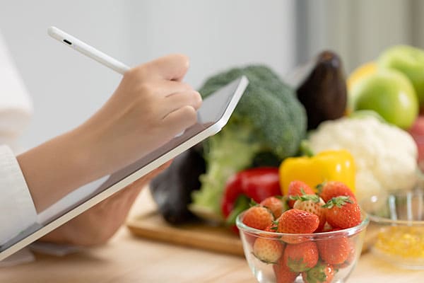 營養師正在使用平板進行健康記錄，周圍擺放著新鮮的水果和蔬菜，象徵著營養管理與健康飲食的重要性。